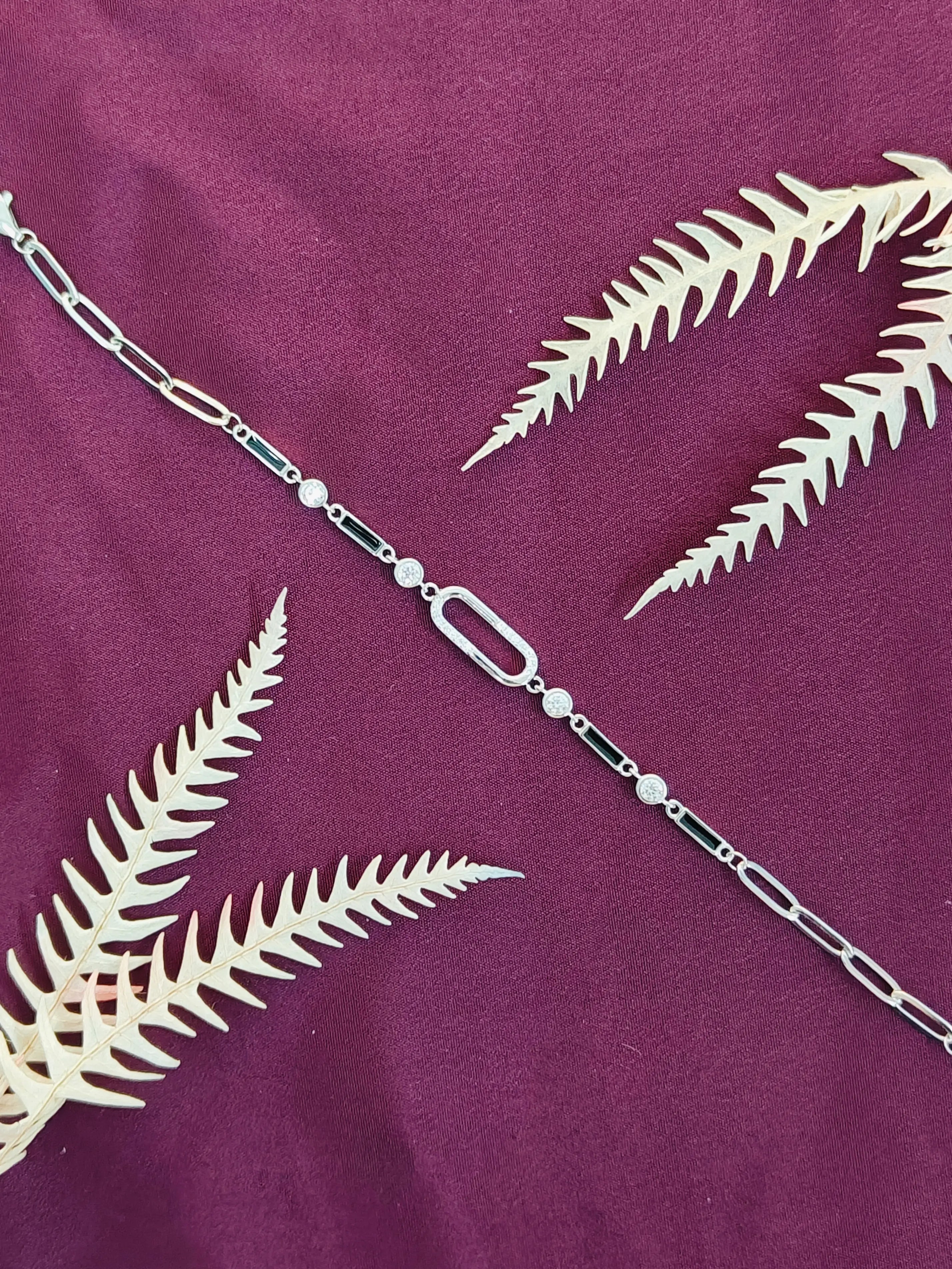 Silver chain necklace with green accents on a purple fabric background